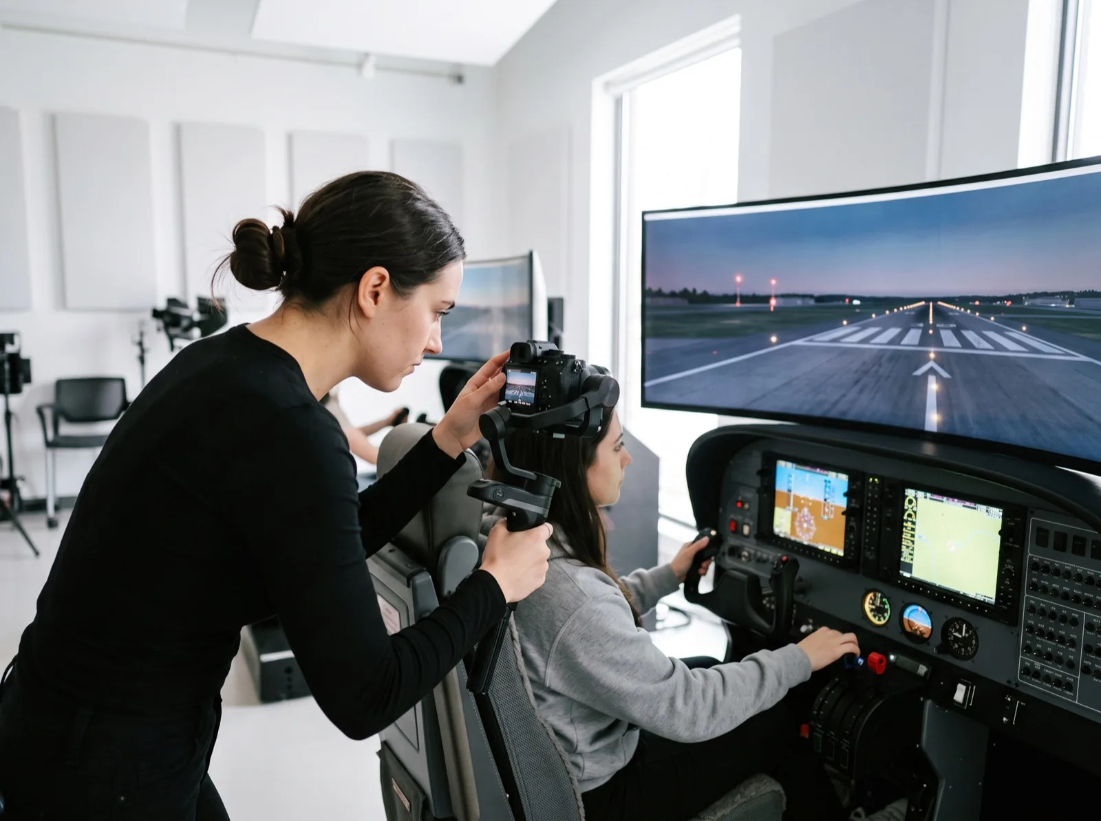 Content creator filming a student flying a glass-cockpit simulator in a bright studio
