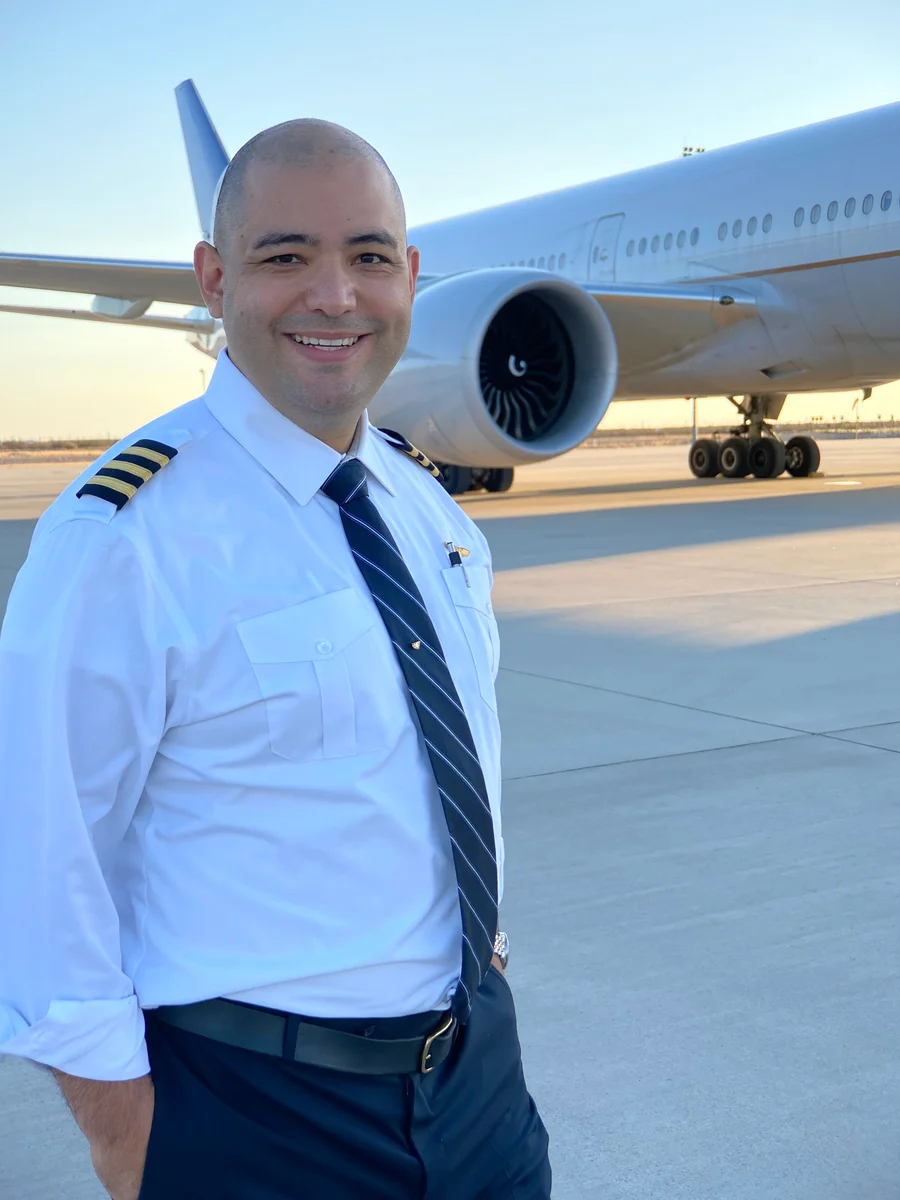 Julian Alarcon in airline captain uniform standing next to a wide-body aircraft on the ramp