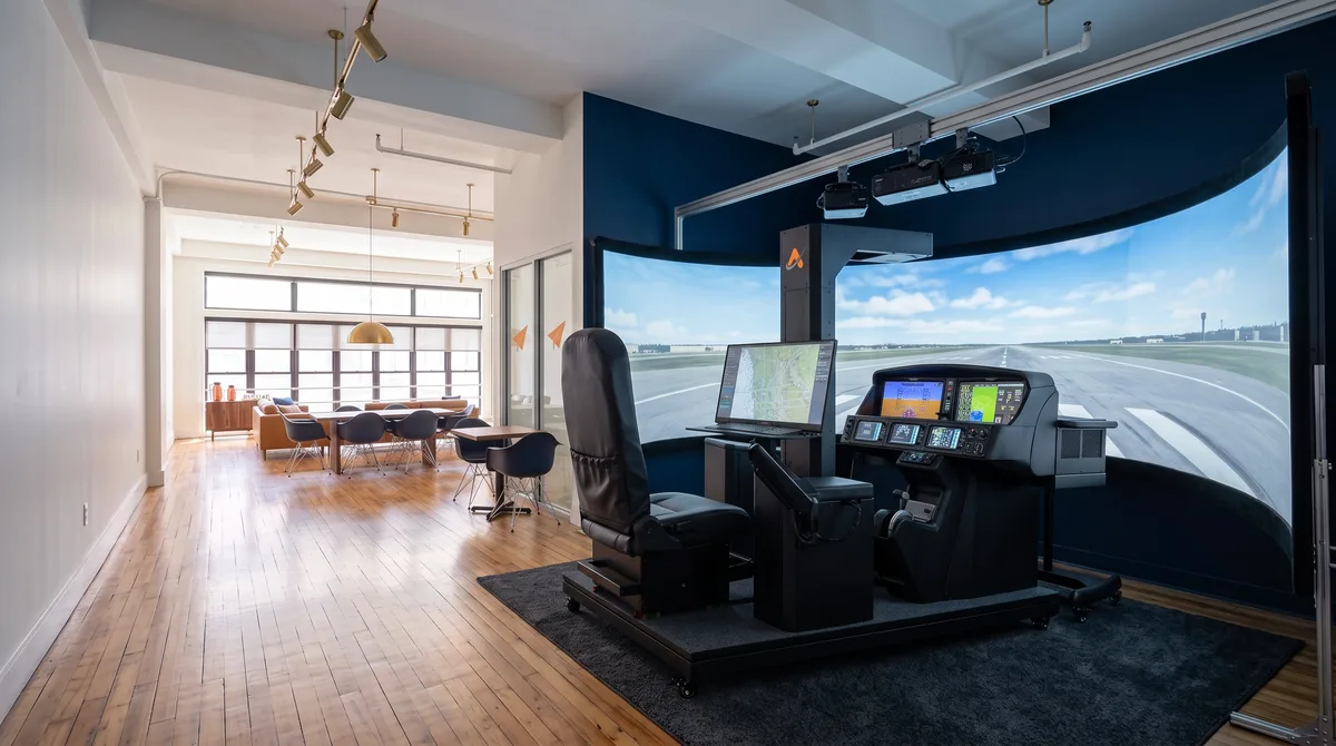 AI-generated rendering of the Cirrus G3000 simulator and its wraparound visual screen in the planned Midtown studio, with the conference and lounge area visible down the room beyond it